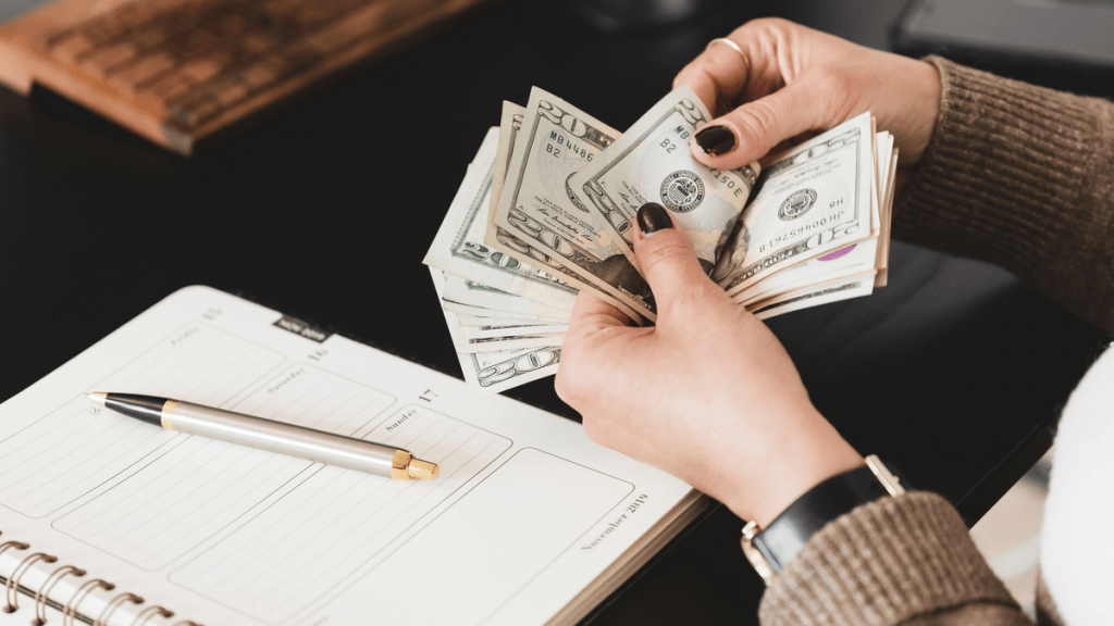 Woman counting cash next to an open planner and pen while setting up a monthly budget