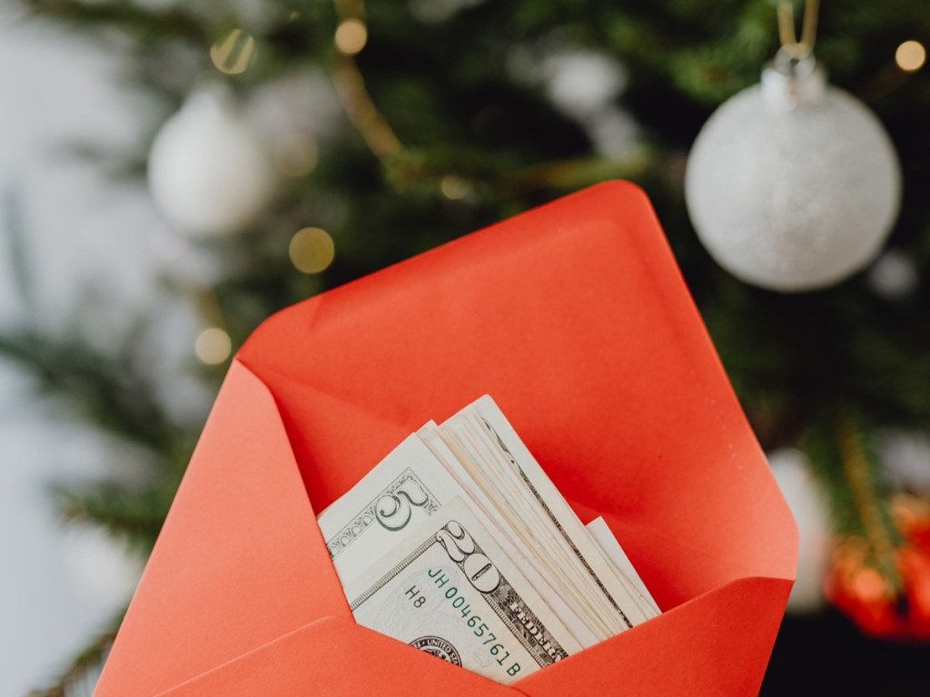 Red envelope with dollar bills in front of a Christmas tree with white ornaments